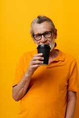 Portrait elderly man in a yellow T-shirt a glass with a drink yellow background