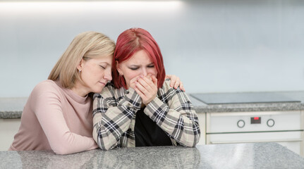 Caring mother hugs and calms her crying teen daughter home. Teenagers problem concept. Empty space for text