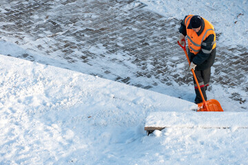 Removing snow from the sidewalk after snowstorm. A road worker with a shovel in his hands and in special clothes cleans the sidewalk and the road from snow. Snowstorm and hurricane in the city. © Pokoman