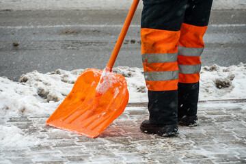 Removing snow from the sidewalk after snowstorm. A road worker with a shovel in his hands and in special clothes cleans the sidewalk and the road from snow. Snowstorm and hurricane in the city.