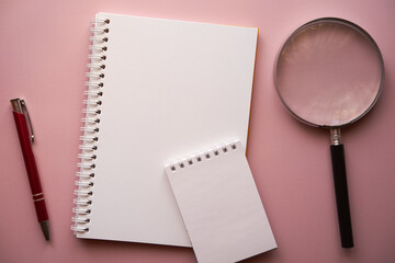 dwa notesy, lupa i długopis na różowym tle - obrazy, fototapety, plakaty
