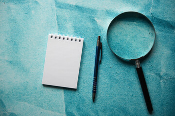 notes, lupa i długopis na papierowym tle 