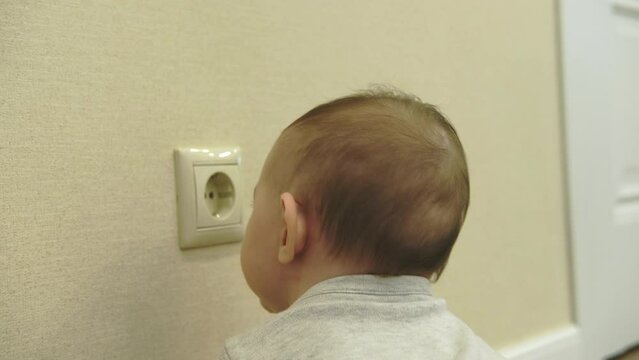 Baby toddler reaches into the electrical outlet on the home wall with his hand. Danger and protection of child fingers from electric shock