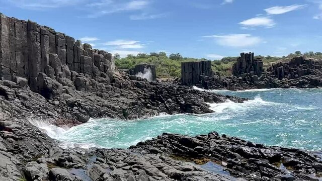 Waves hitting the sea rocks, Coastal landscape with sandy wall, rocky rock formations and outdoor tall columns on the seaside cove of bombo, kiama quarry, australia
