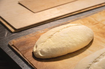 A raw loaf of French bread lies on a wooden board. Preparing before baking artisan bread