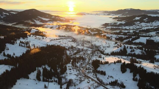 The extraordinary Carpathian valley with snow-capped hills and mountains covered with evergreen spruce forests against the backdrop of a warm bright fiery sunset