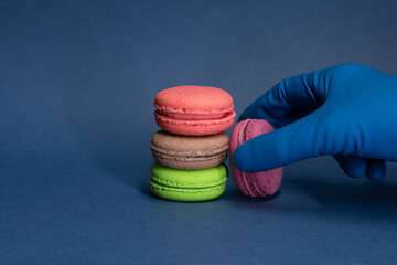 Person in blue gloves reaches for multi colored  french macarons lying on a blue background. Pastry-shop. Confectionery theme.