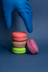 Person in blue gloves reaches for multi colored  french macarons lying on a blue background. Pastry-shop. Confectionery theme.