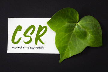 green leaf and a white note paper with acronym CSR Corporate Social Responsibility on black...