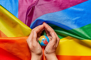 Hands with globe on rainbow flag, pride day concept