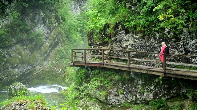 Young female photographer in colourful jacket hiking a trail along a clear river through the Vintgar Gorge in Slovenia