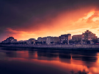 Orange stormy sunset and maroon colors in an illuminated city next to the Ebro river.