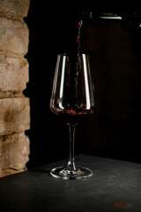 close-up of wine glass into which red wine is poured from a bottle.