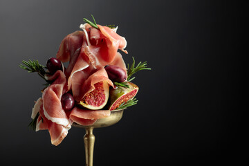 Prosciutto with figs, rosemary, and red olives in an old brass dish.