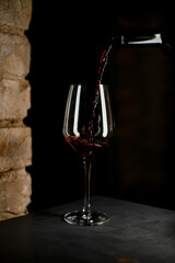 Great view of wine glass into which red wine is poured from a bottle.