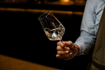 hand of man gently holds tilted transparent wine glass with a drink