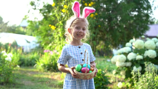 a little blonde girl with bunny ears holding a basket of painted Easter eggs in her hands and laughing, the concept of a religious holiday
