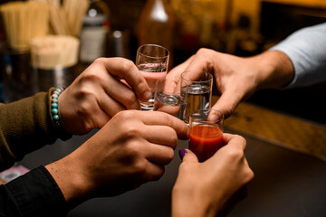 Close-up of male hands cheers with glasses of vodka and liqueur - obrazy, fototapety, plakaty