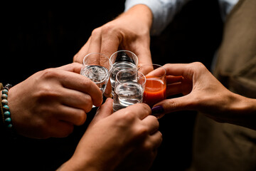 Close-up view of male hands cheers with glasses of vodka and liqueur - obrazy, fototapety, plakaty
