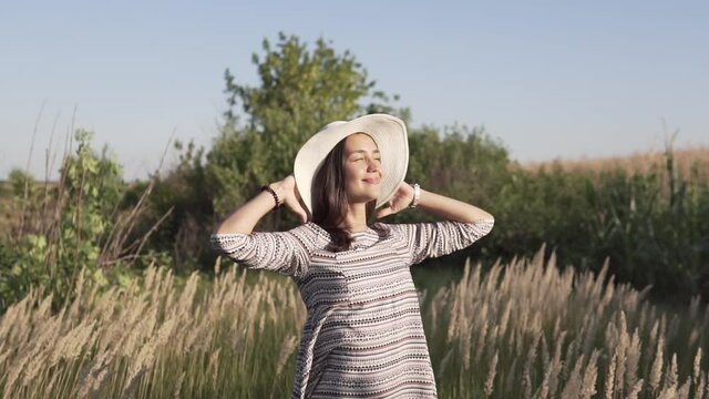 Beautiful young girl in a straw hat.She stands in a field and looks at the setting sun.Slow motion