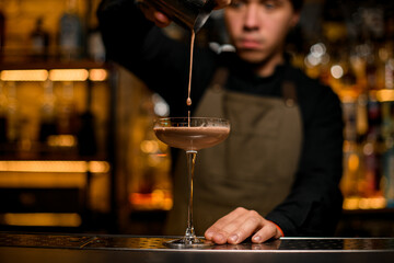 beautiful cocktail glass into which drink is being poured from shaker