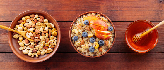 Tasty oatmeal with berries, nuts and apples on wooden table. Bowl of oatmeal porridge with blueberries and honey. Healthy breakfast. Top view