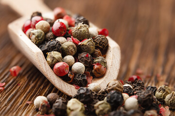 A mixture of red white green and black peppercorns in a wooden scoop