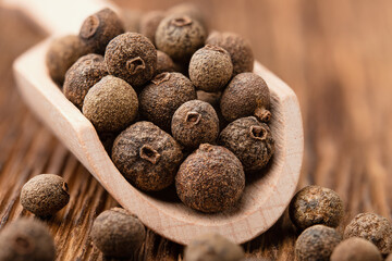 Allspice peas in a wooden scoop close up