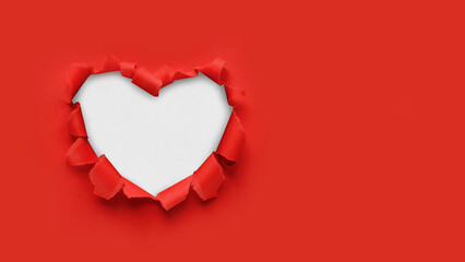 Naklejka na ściany i meble A paper hole with torn edges on a red background. Through paper. A ragged hole in the shape of a heart. Valentine's day. A symbol of love, romantic relationships. International Women's Day.