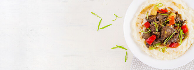 Fried chicken liver with apples, sweet pepper and onions with mashed potatoes  a bowl on white wooden table. Top view, banner