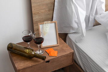 Empty bottle with glasses of wine and used condom on table in bedroom