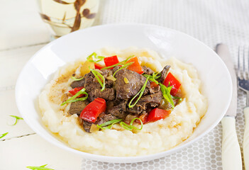 Fried chicken liver with apples, sweet pepper and onions with mashed potatoes  a bowl on white wooden table.