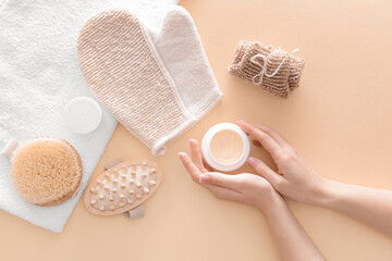 Female hands with cosmetic cream and bathing supplies on color background