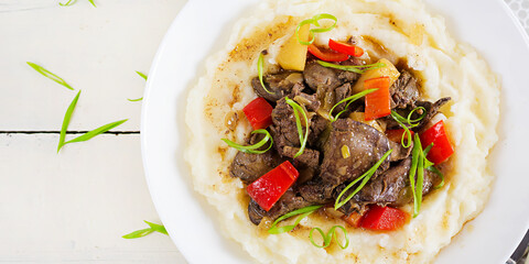Fried chicken liver with apples, sweet pepper and onions with mashed potatoes  a bowl on white wooden table. Top view, overhead