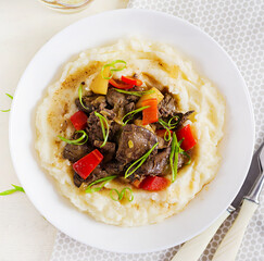 Fried chicken liver with apples, sweet pepper and onions with mashed potatoes  a bowl on white wooden table. Top view, overhead