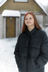 A brown-haired girl with long hair stands on the street in winter smiling