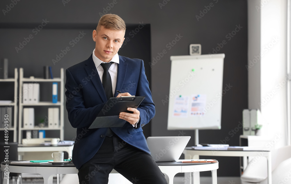 Sticker Handsome businessman writing on clipboard near table in office