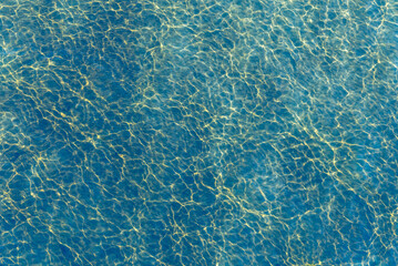 The surface of the water with golden reflections of the sun on a blue surface with small waves - sea surface, top view