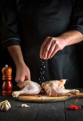 Cook prepares raw chicken legs in the restaurant kitchen. The chef adds salt to the chicken leg before baking. National dish