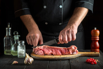 Professional chef cuts meat with a knife before baking. Spices on kitchen table in a restaurant for preparing a delicious lunch.