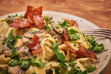 Fettuccine with mushroom sauce, fried bacon and fresh parsley in a plate, close-up - classic italian pasta