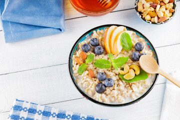 Oatmeal bowl and honey on a white boards. Oatmeal porridge with blueberries, apple slices and fresh mint. Healthy breakfast. Top view. Copy space