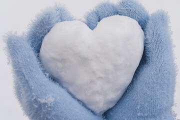 Closeup cozy female hands in blue fluffy mitten with heart of snow in winter day. Love concept....