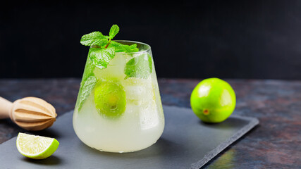 Mojito cocktail, lime and wooden juicer on a dark background. Summer cocktail mojito with lime and mint on a slate board. Summer drink concept