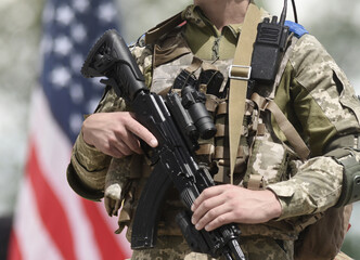 Soldier with assault rifle and US flag at the background. US military support Ukraine.