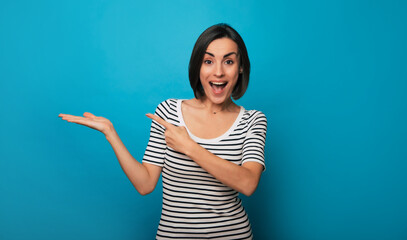 Photo of an excited attractive brunette woman in casual wear while she pointing at something advert on her arm and isolated on blue background