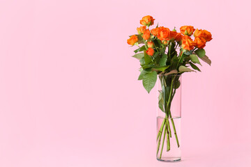 Vase with beautiful orange roses on pink background