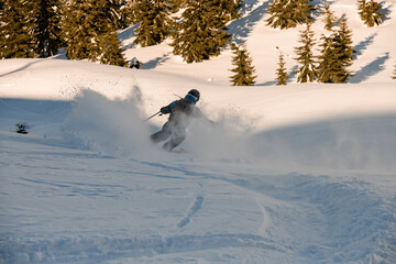Rear view of freerider speedly sliding down mountain slope and the splashing snow around him
