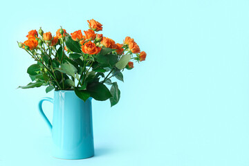 Jug with beautiful orange roses on blue background