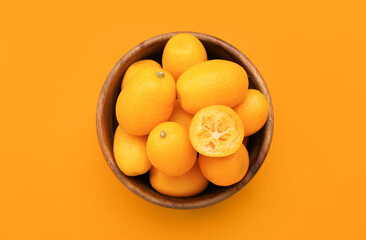 Bowl with tasty kumquat fruits on orange background